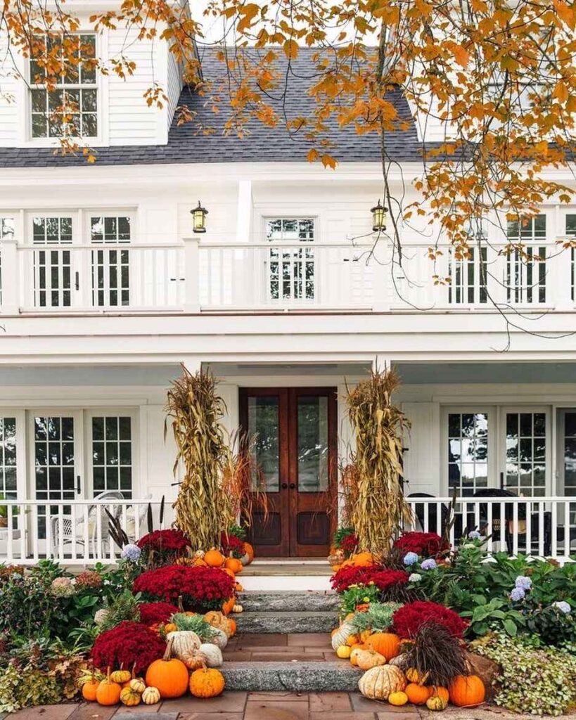 White farmhouse, cornstalk-framed door, pumpkins, mums