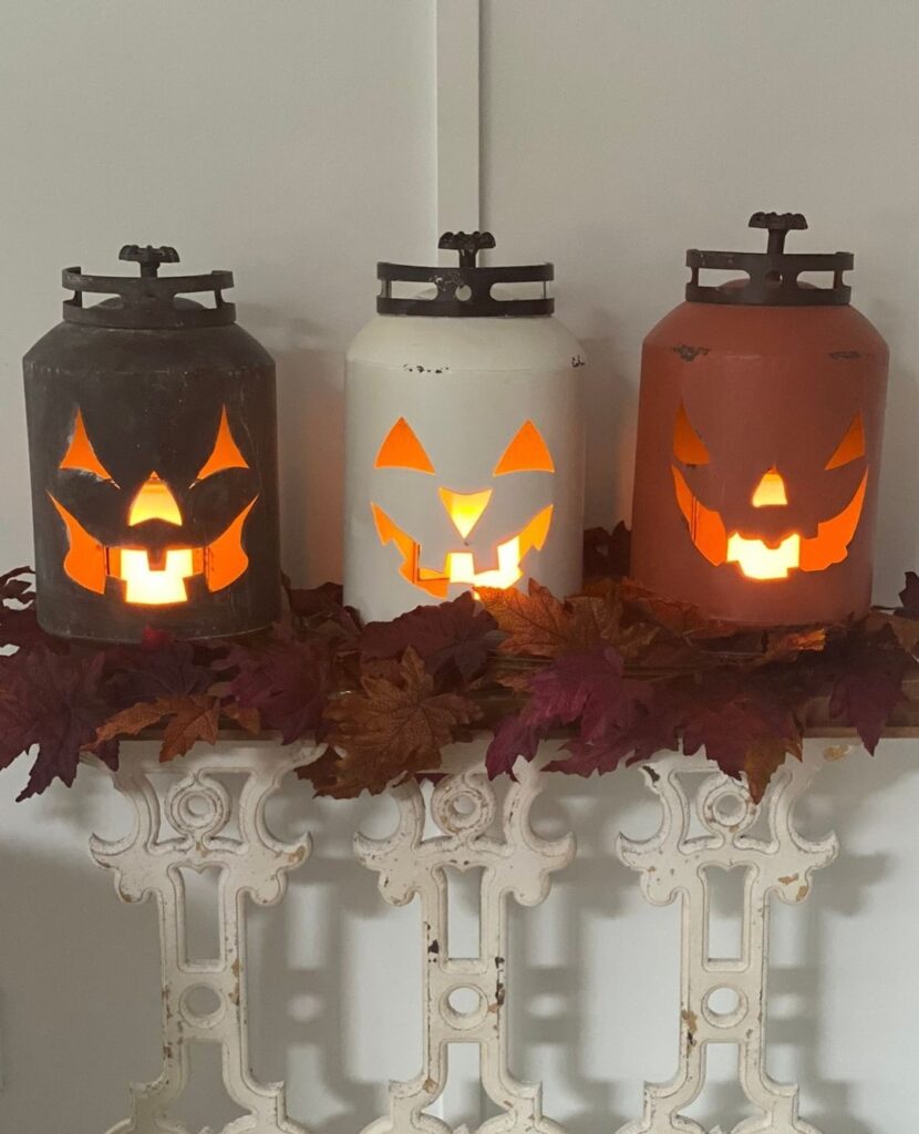 Three illuminated canister pumpkins on shelf