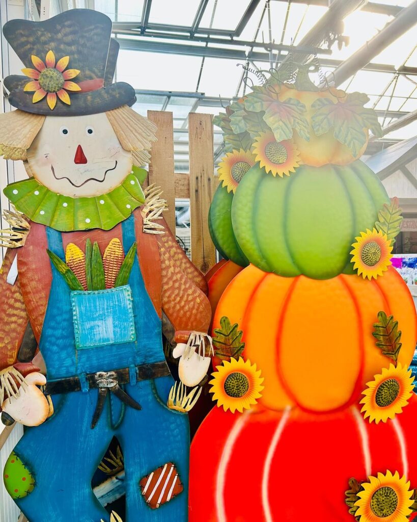 Colorful scarecrow next to stacked pumpkins with sunflowers