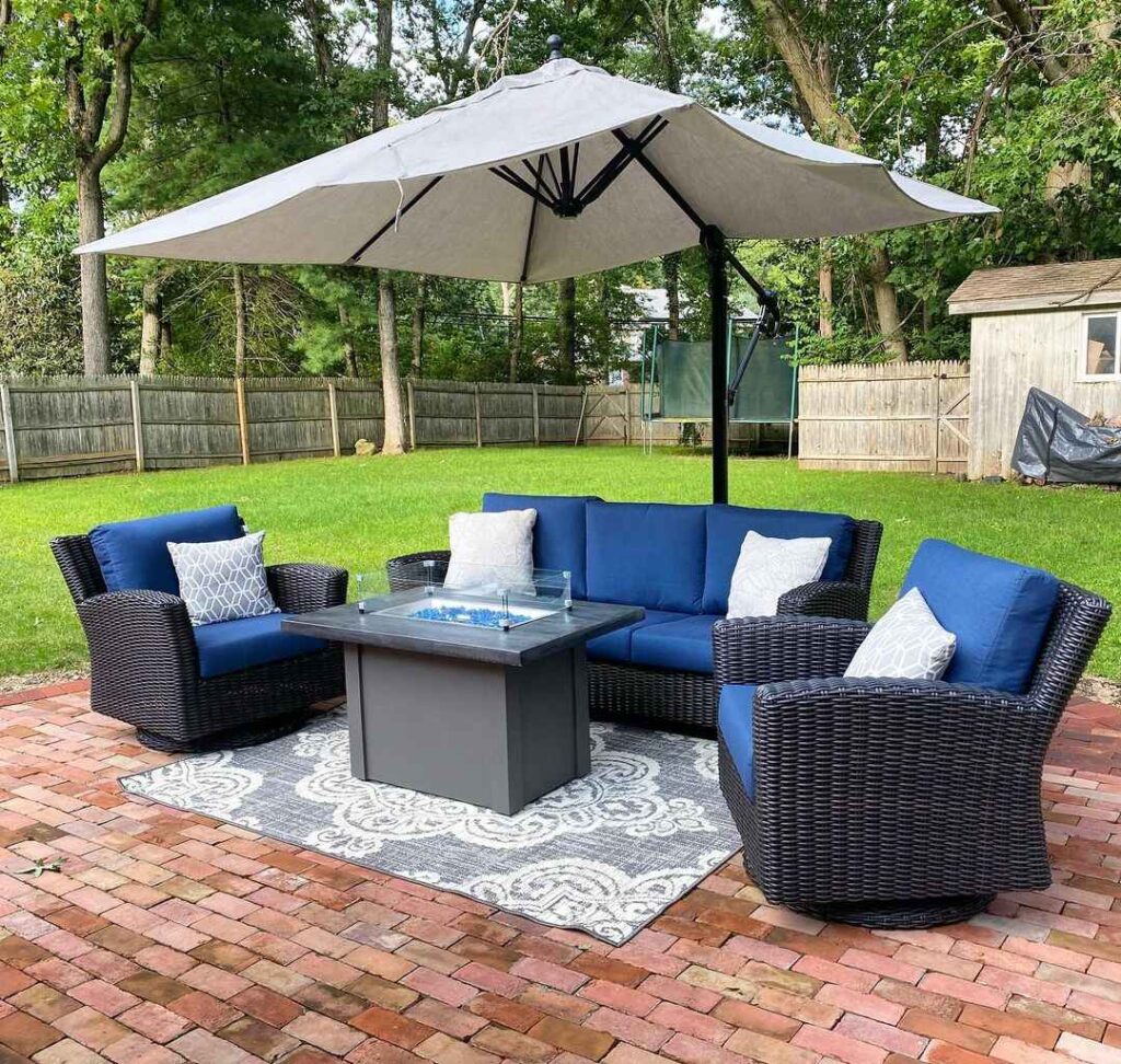 Navy wicker patio set with fire table on brick patio under large umbrella