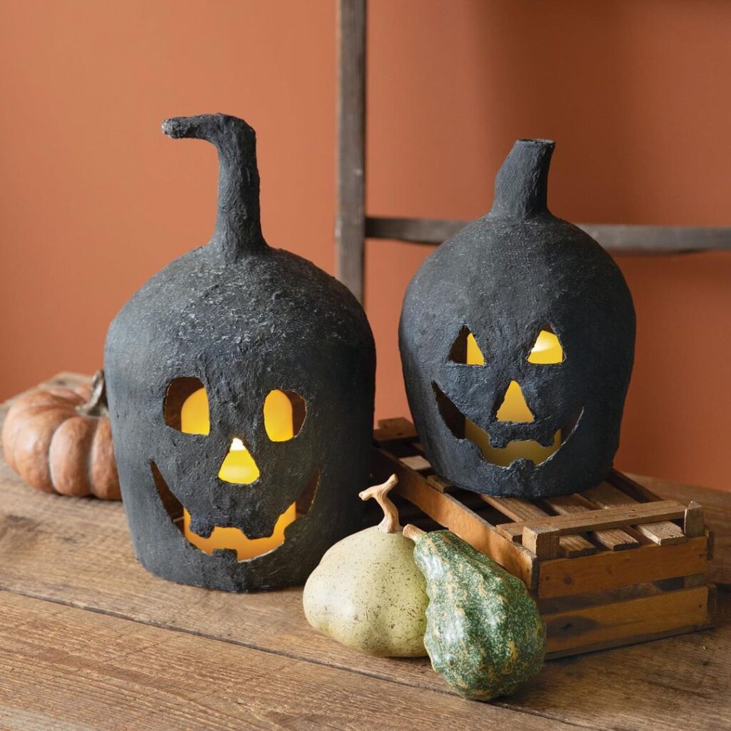 Two black ceramic pumpkin lanterns with glowing faces on wooden surface.