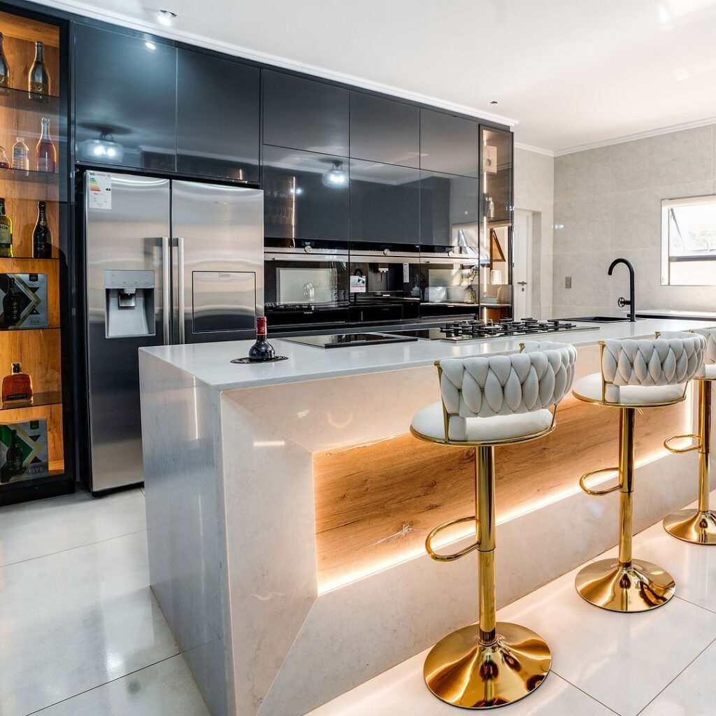 Modern black and white kitchen with illuminated bar and gold stools.