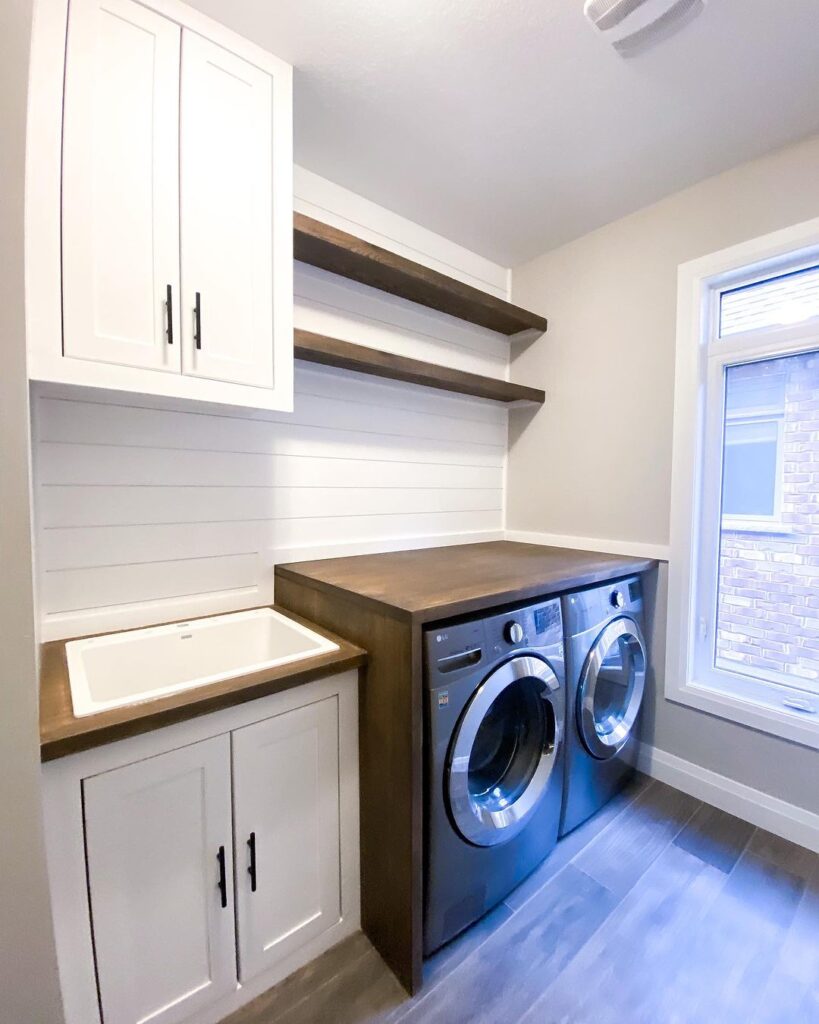 Modern laundry room with white cabinets wooden accents and metallic appliances