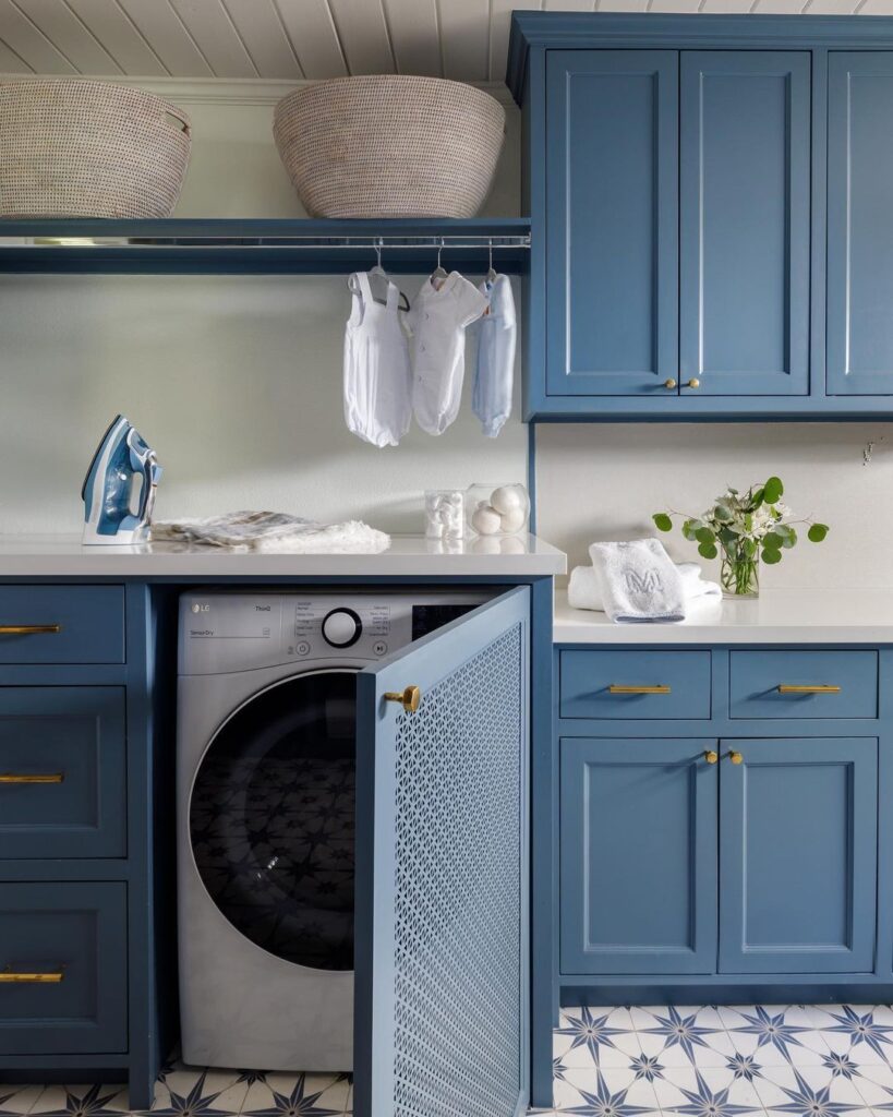 Blue laundry room with hidden washer and hanging baby clothes.