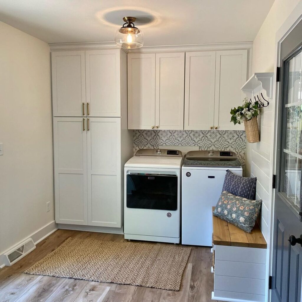 Bright laundry room with white cabinets, top-loading appliances, and built-in bench seating.