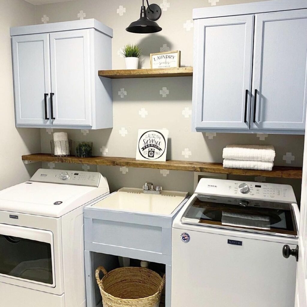 Farmhouse laundry room with gray cabinets wooden shelves and patterned wallpaper