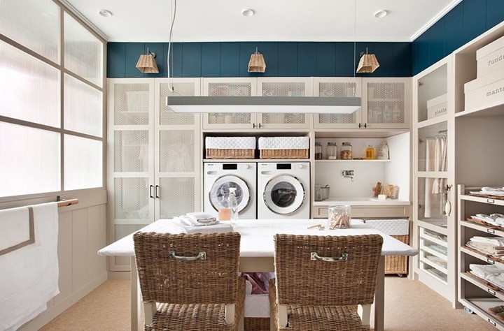 Laundry room with teal wall white cabinets and central table with rattan chairs.