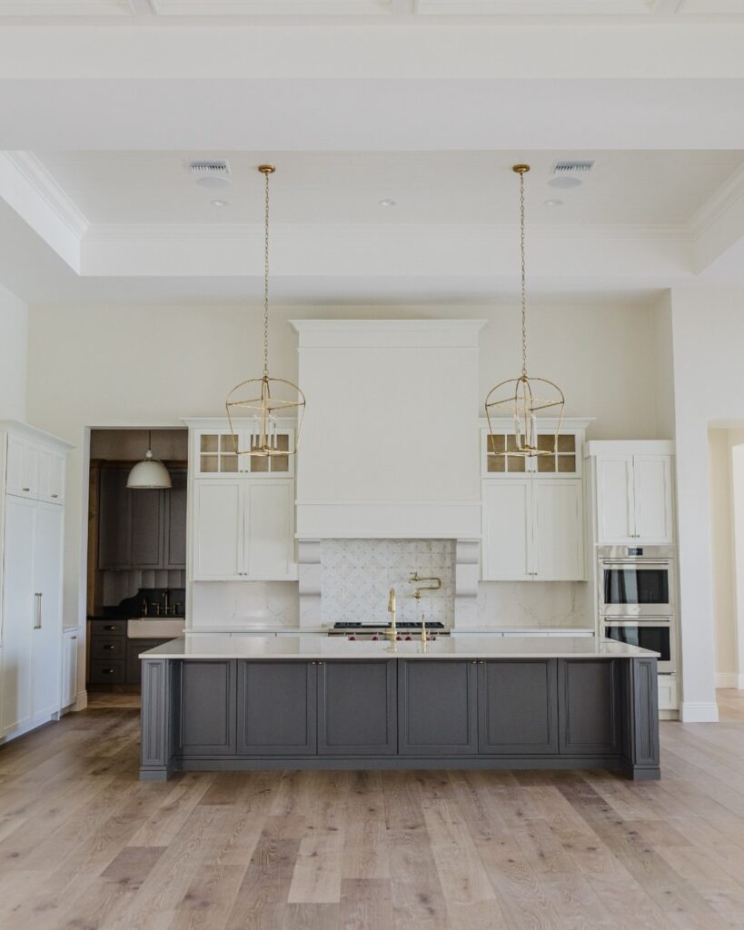 Spacious beige kitchen with white cabinets, gray island, and brass accents.