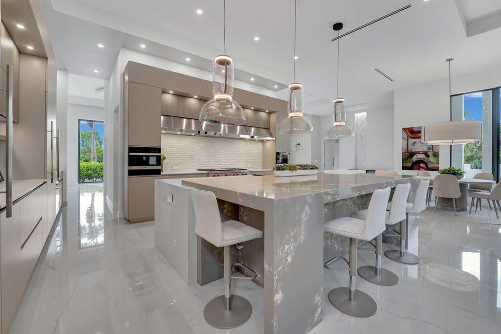 Modern white kitchen with large marble island and glass pendant lights.