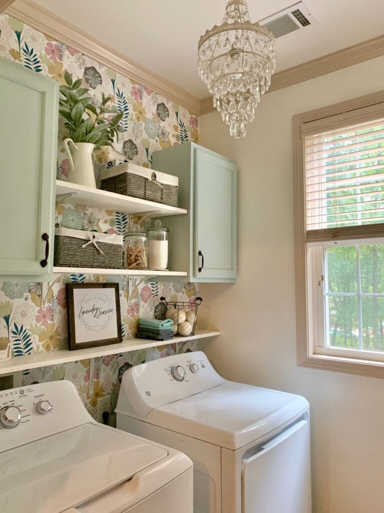 Elegant laundry room with floral wallpaper crystal chandelier and mint cabinets