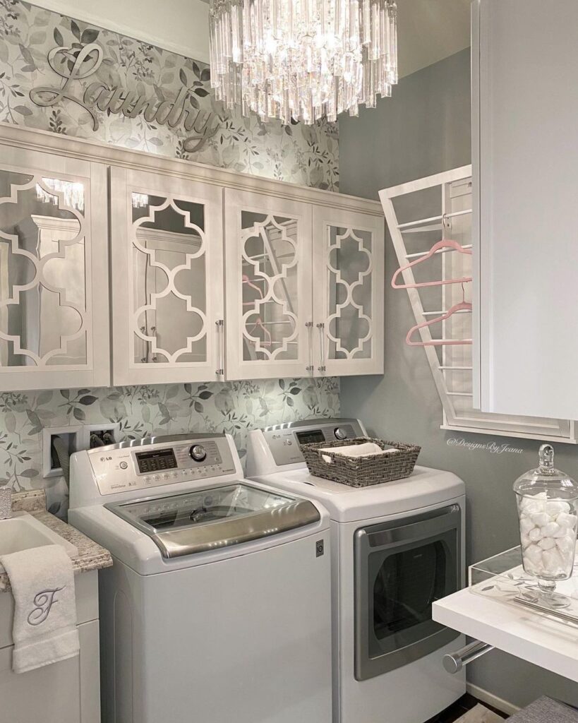 Elegant laundry room with crystal chandelier, ornate cabinets, and top-loading washer and dryer.