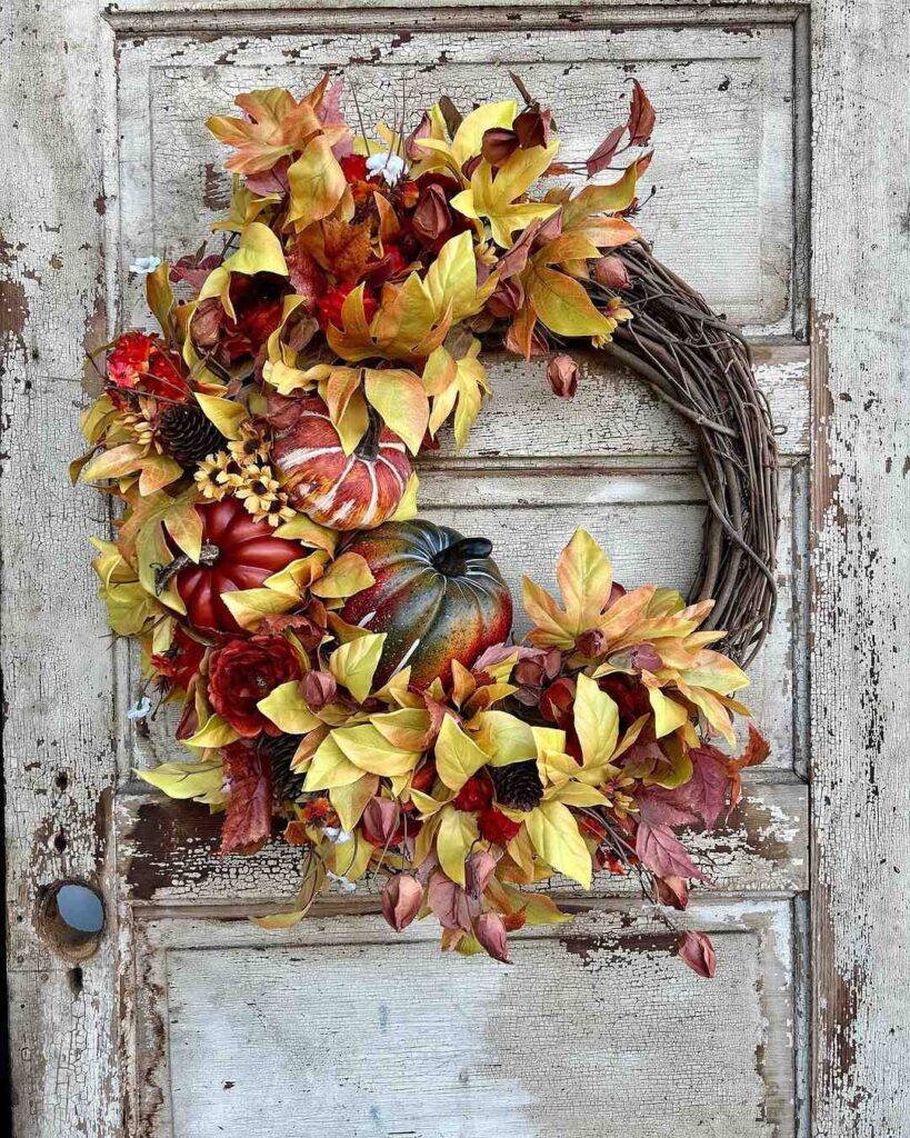 Fall wreath with yellow leaves pumpkins and flowers on distressed white door