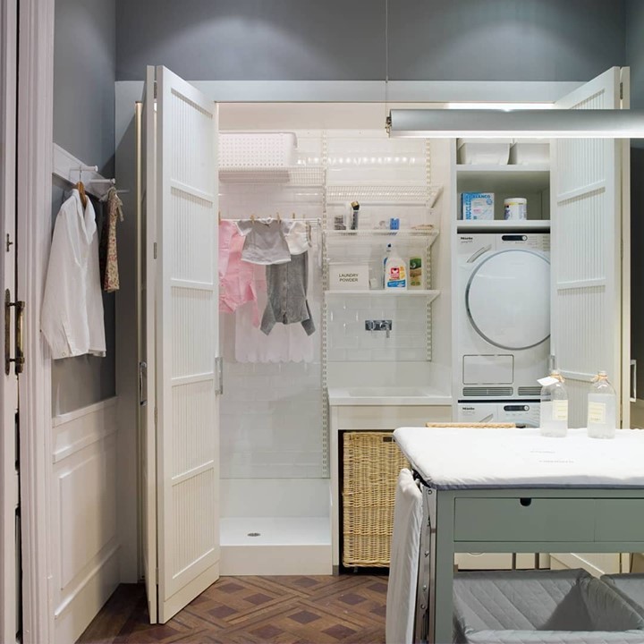 Concealed laundry room with white pegboard walls stacked washer dryer and folding table outside.