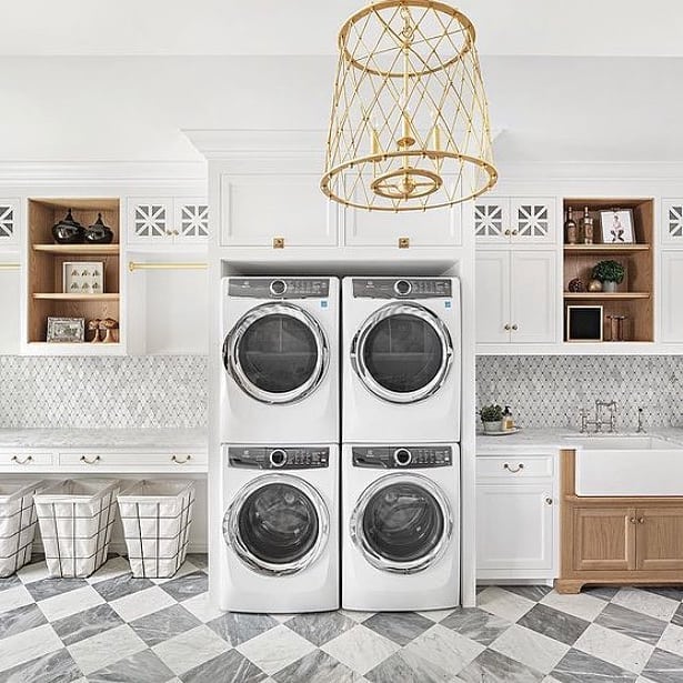 Chic laundry room with stacked washers, gold chandelier, and checkered floor.