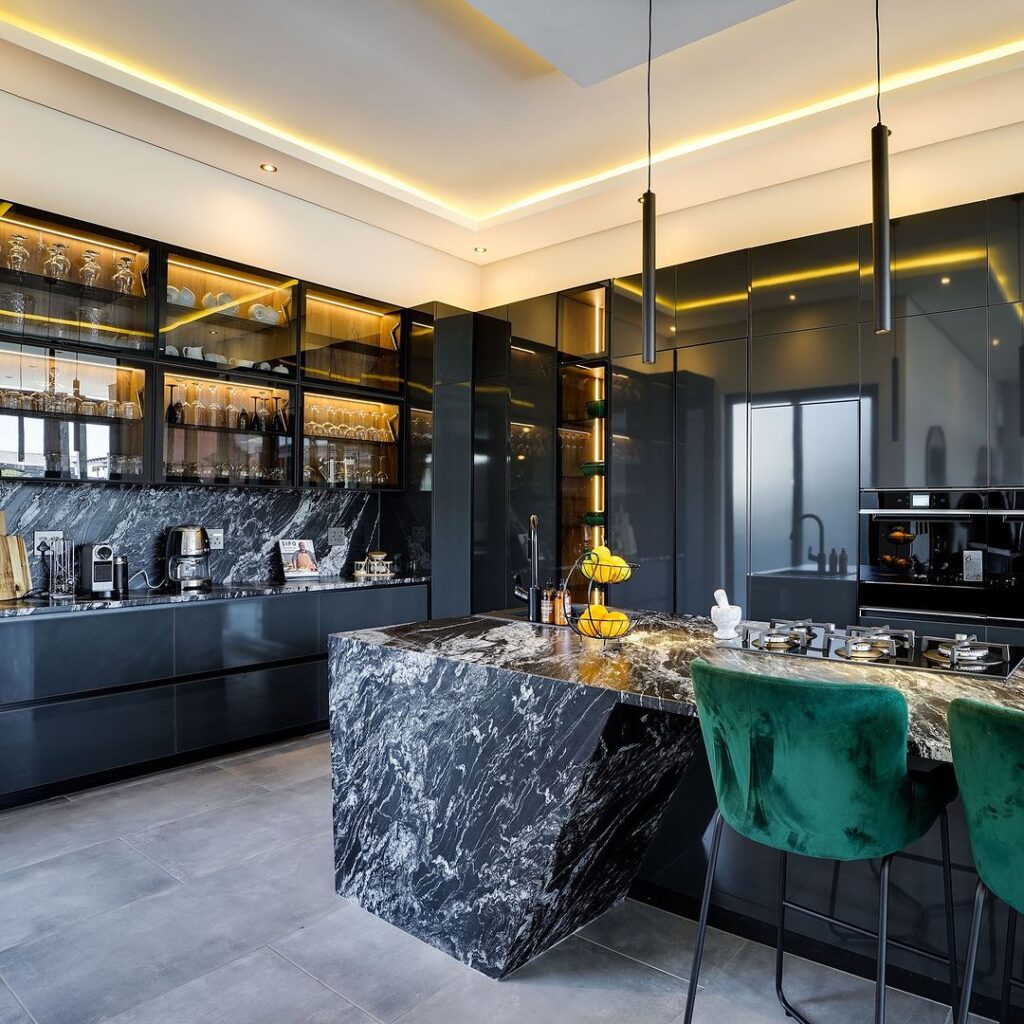 Luxurious dark kitchen with marble island and green stools.