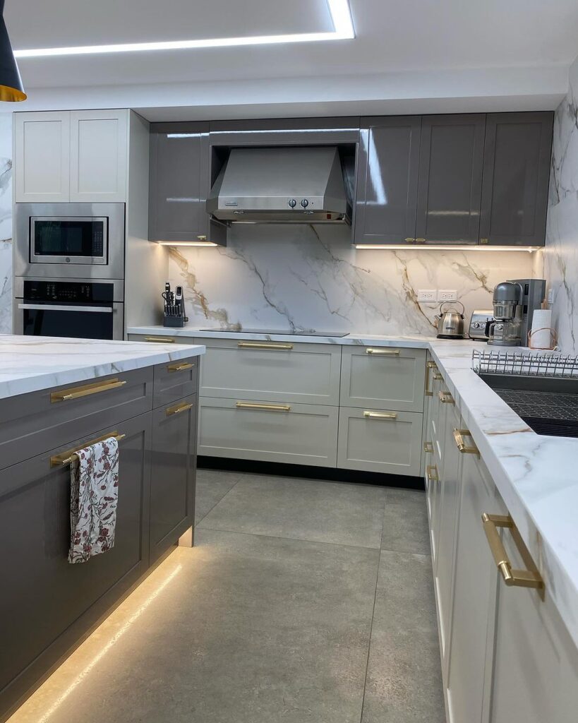 Modern two-tone kitchen with marble backsplash and gold accents.