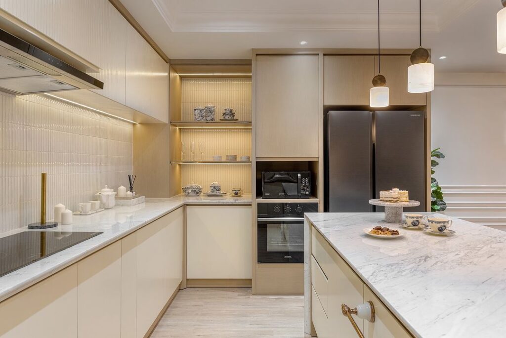 Modern cream kitchen with marble countertops and pendant lights.