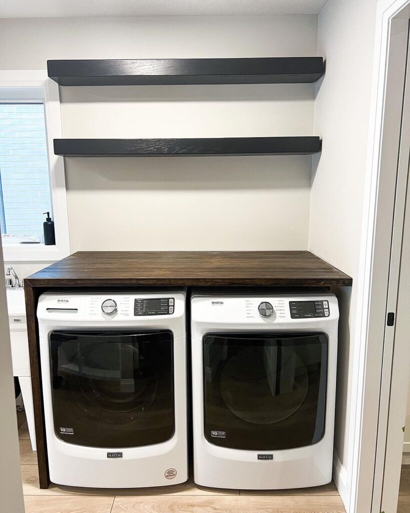 Laundry room with white appliances wooden counter and black shelves