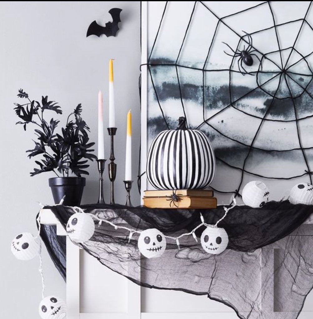 Sophisticated black-white Halloween decor on mantel with pumpkin and spiderweb.