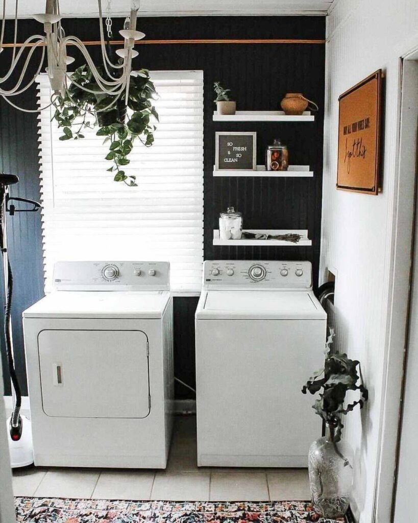 Stylish laundry room with black accent wall top-load appliances and chandelier.