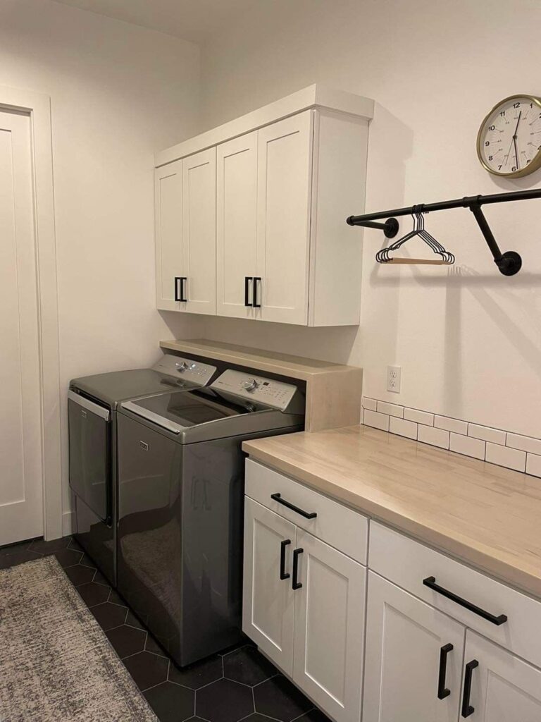 Modern laundry room with white cabinets dark appliances and hanging rod