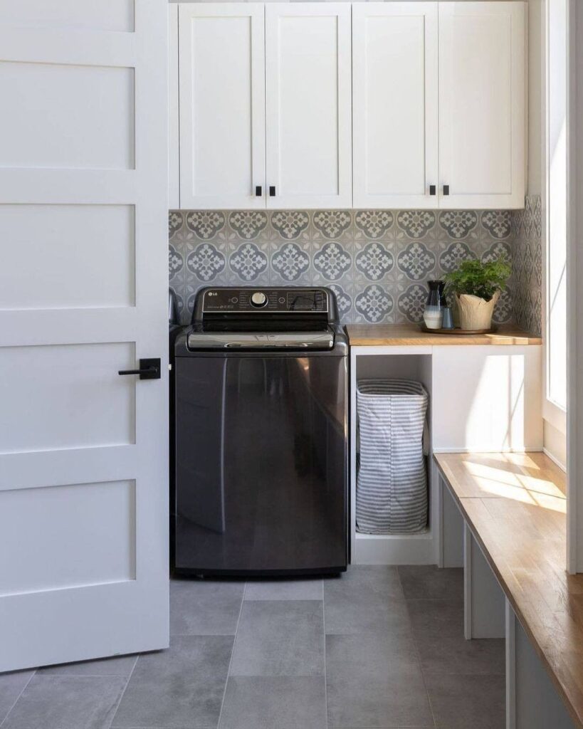 Stylish laundry room with black top-load washer Moroccan tile and white cabinets.