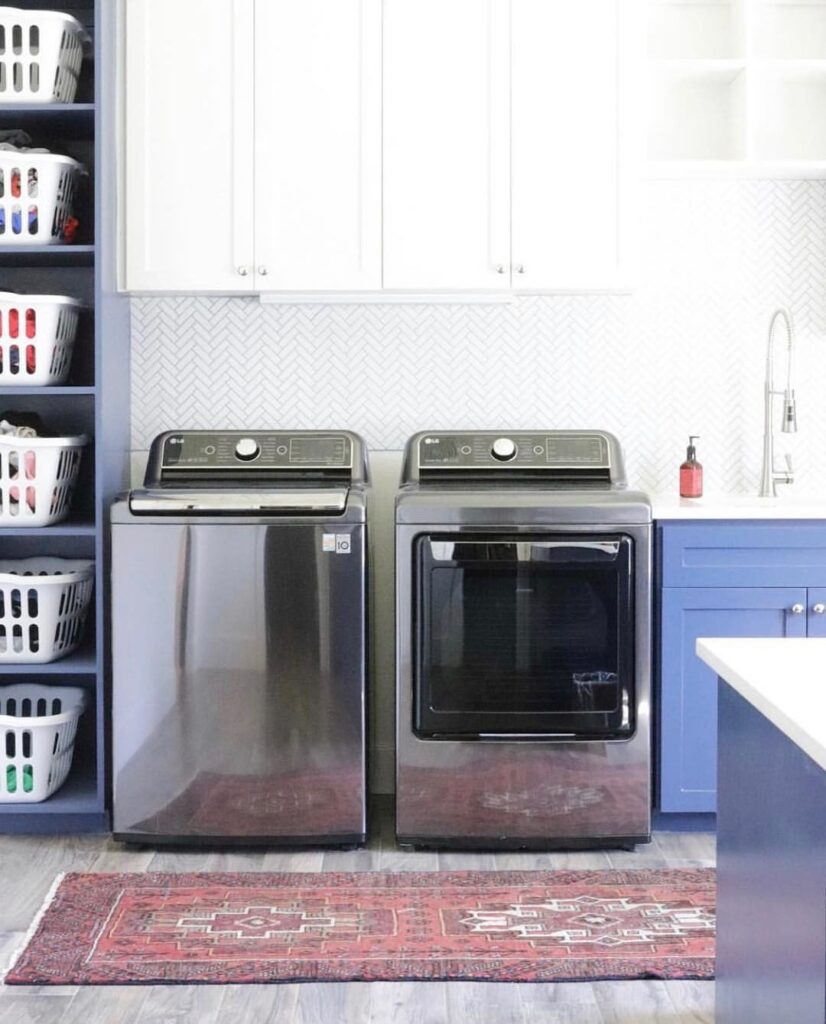 Laundry room with top-loading washer, blue cabinets, and organized shelving for baskets.