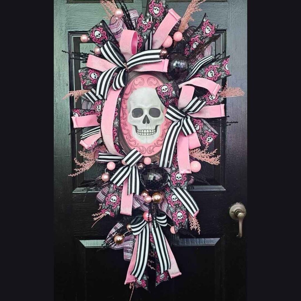 Skull-centered Halloween wreath with pink, black, and striped ribbons on dark door.