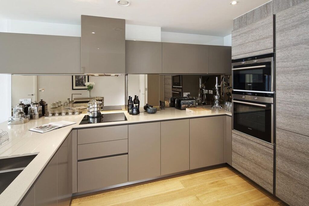 Modern taupe kitchen with mirrored backsplash and sleek appliances.