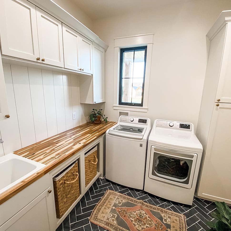 Bright laundry room with wooden counter top-load machines and patterned floor.