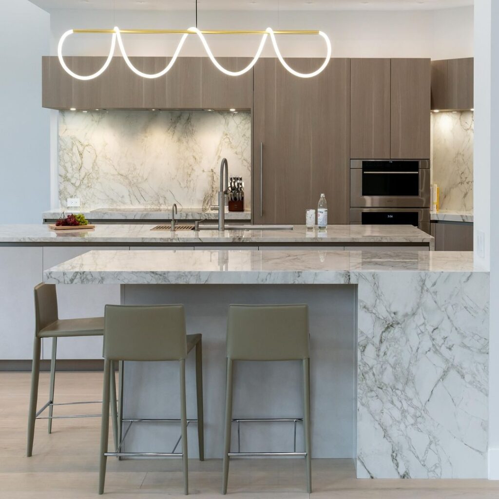 Modern kitchen with looped light fixture and marble surfaces.