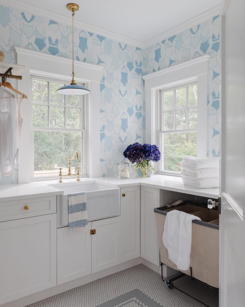 Bright laundry room with blue swimsuit wallpaper and white cabinets.