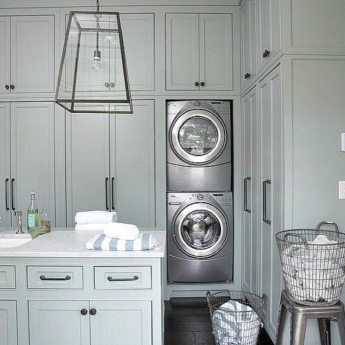 Elegant gray laundry room with built-in cabinets and stacked machines.