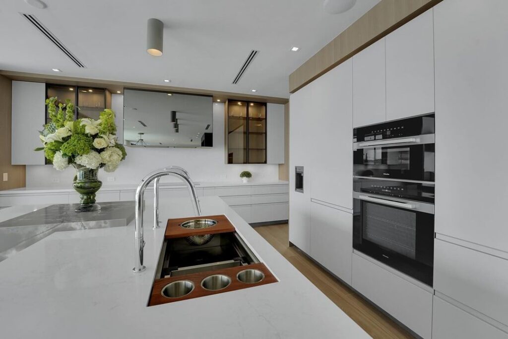 Modern white kitchen with floral centerpiece and wooden sink details.