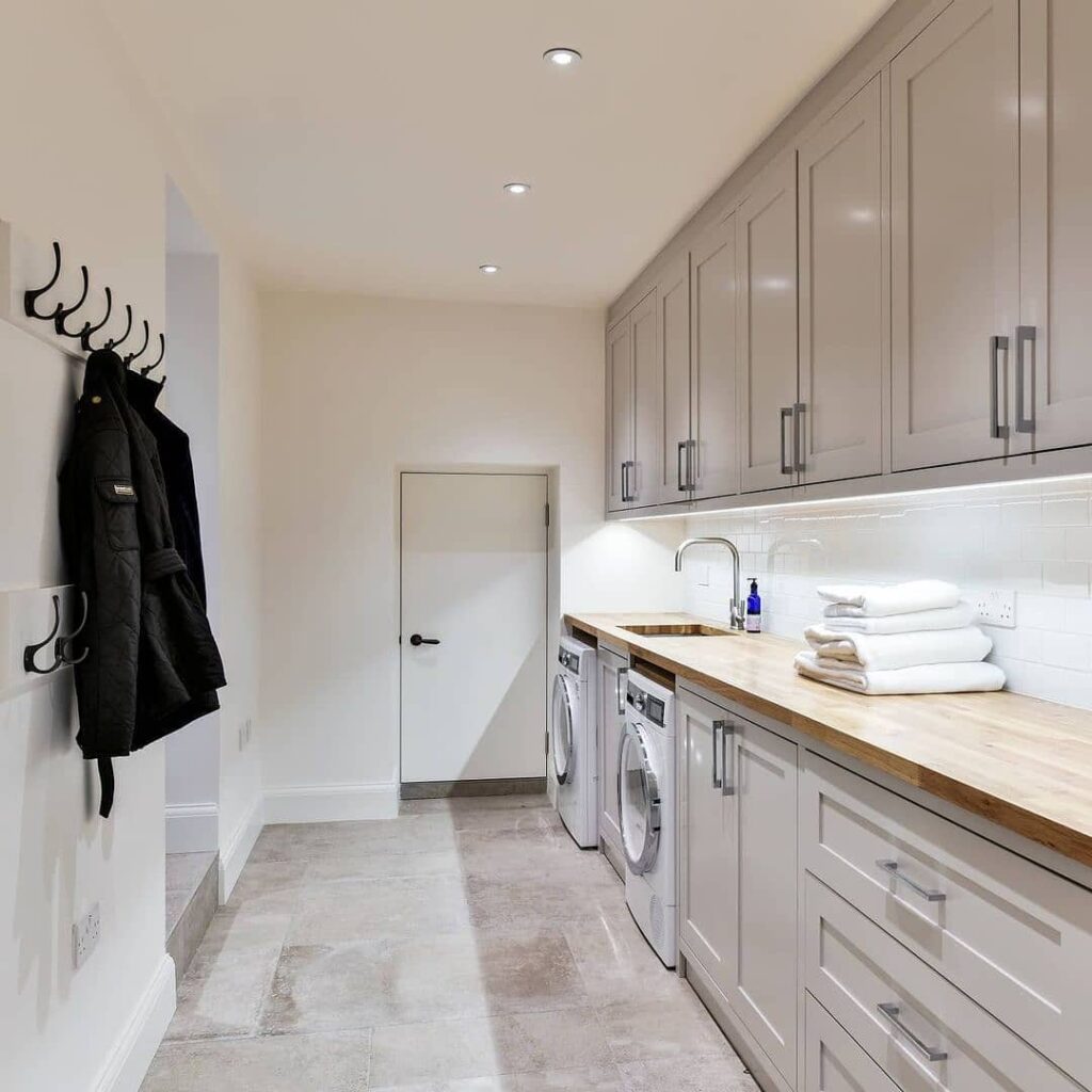 Long narrow laundry room with gray cabinets and wooden countertop.