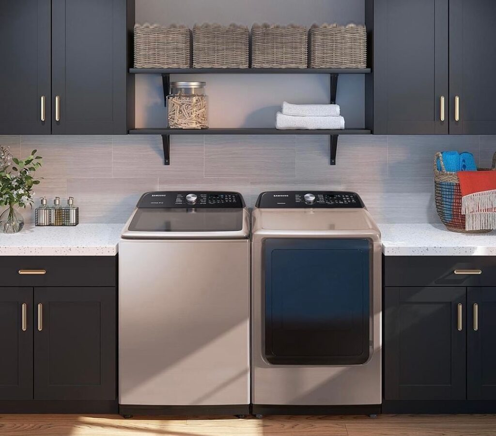 Modern laundry room with dark cabinets, metallic top-loading washer and dryer, and organized shelving.