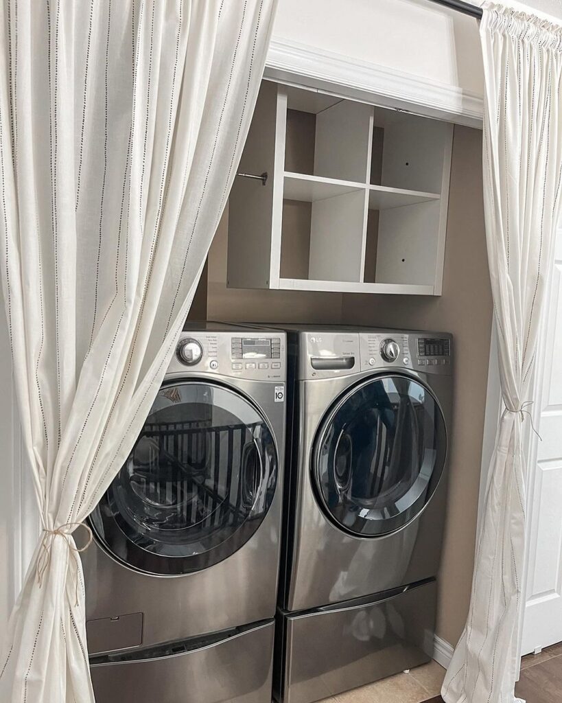 Laundry machines behind white curtains with overhead storage shelves