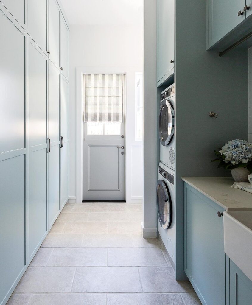 Mint green laundry room with stacked appliances and ample storage.