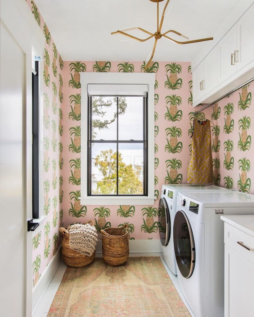 Laundry room with pink pineapple wallpaper and window view.