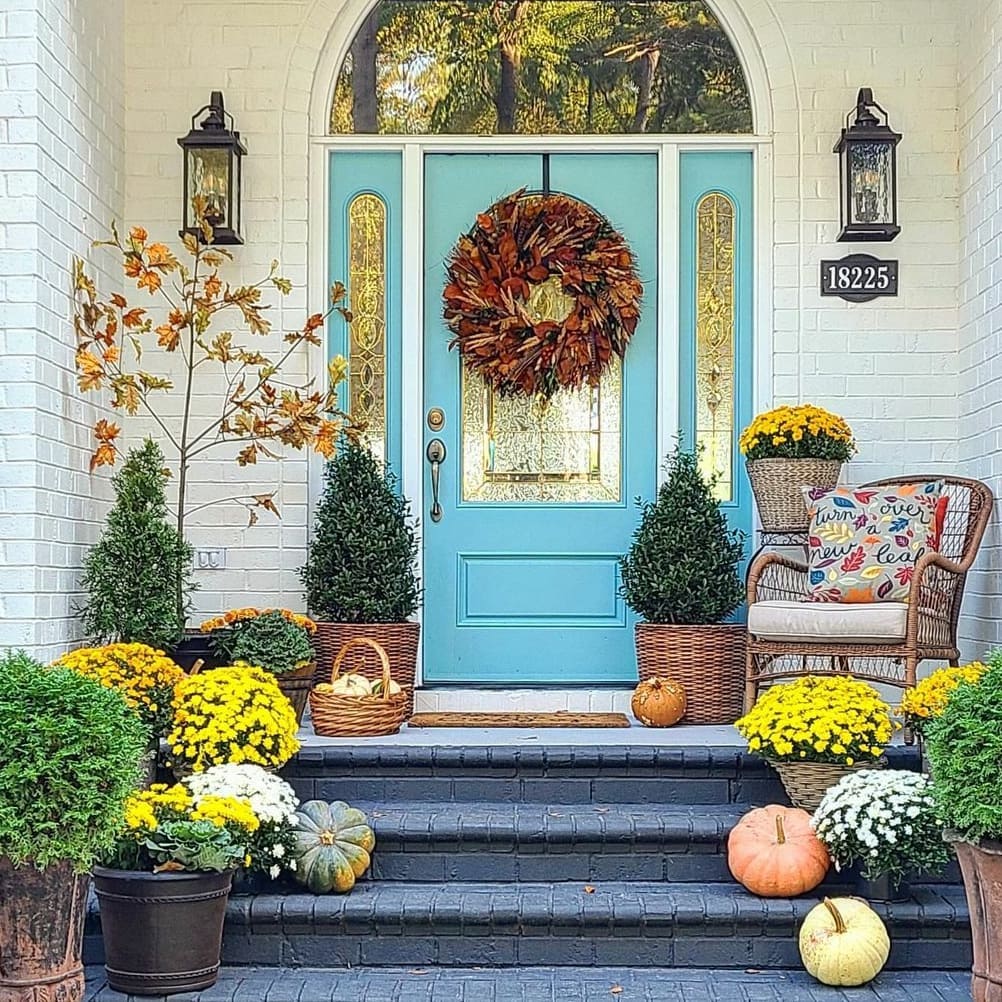 Turquoise door with fall wreath surrounded by mums pumpkins and autumn decor