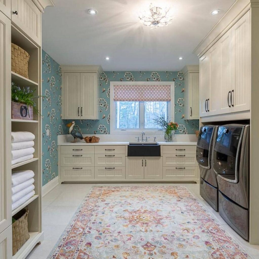 Teal wallpapered laundry room with white cabinets and patterned rug.