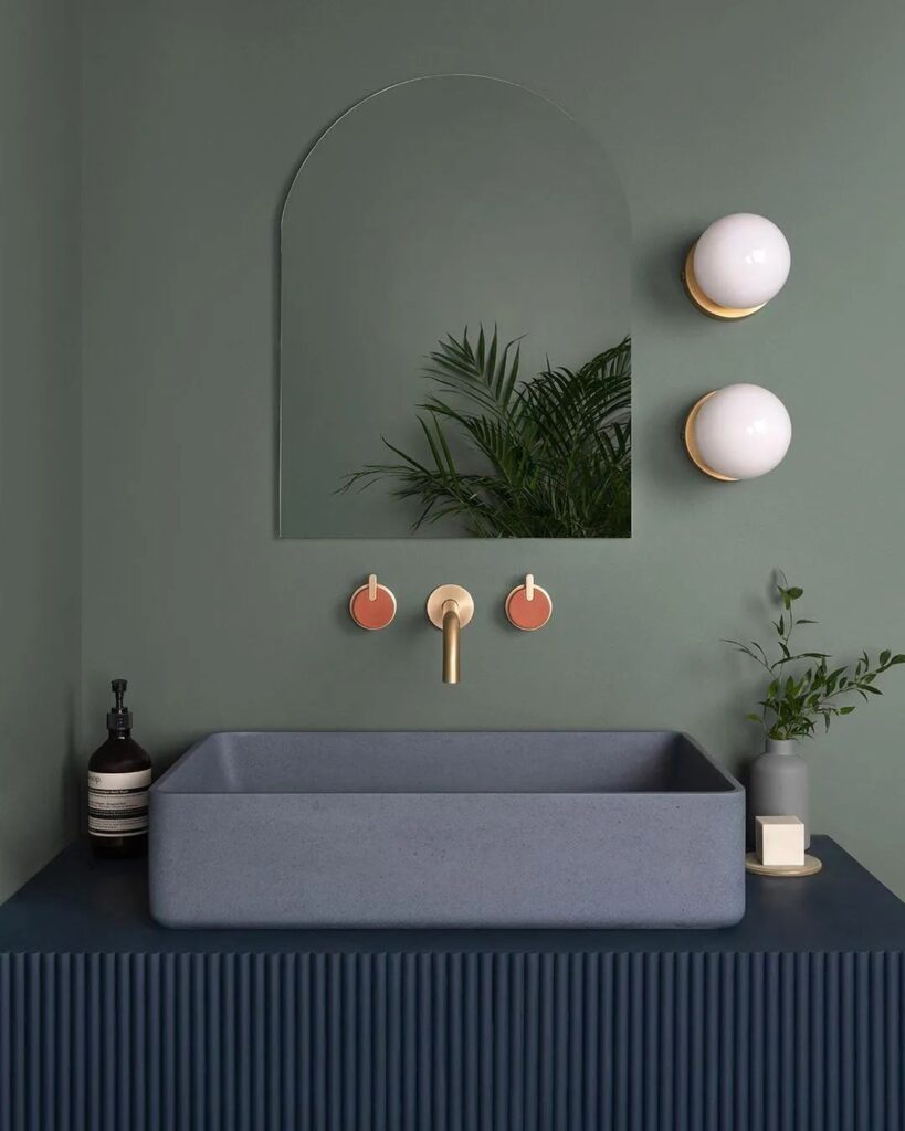 Minimalist green bathroom with arched mirror, modern sink.