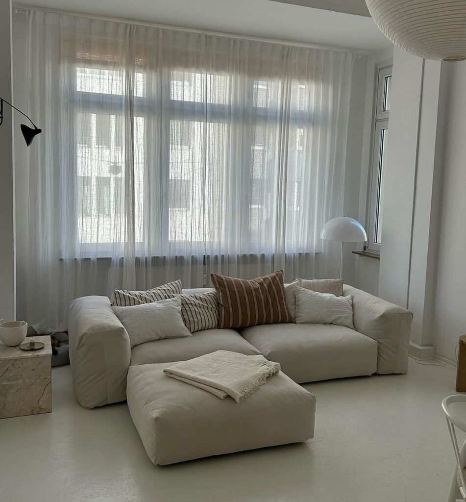 Bright minimalist living room with white sofa and sheer curtains.