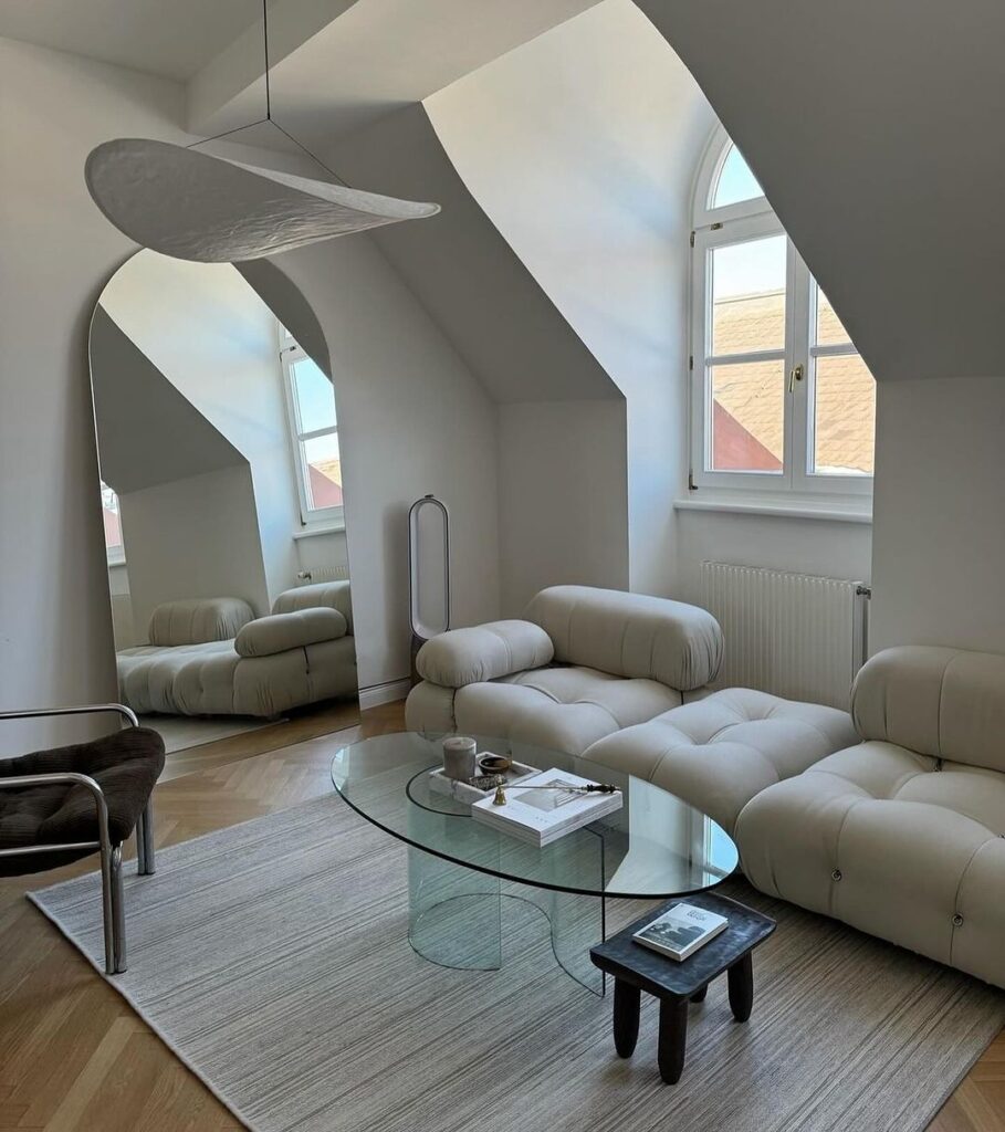 Bright attic living room with white modular sofa and glass table