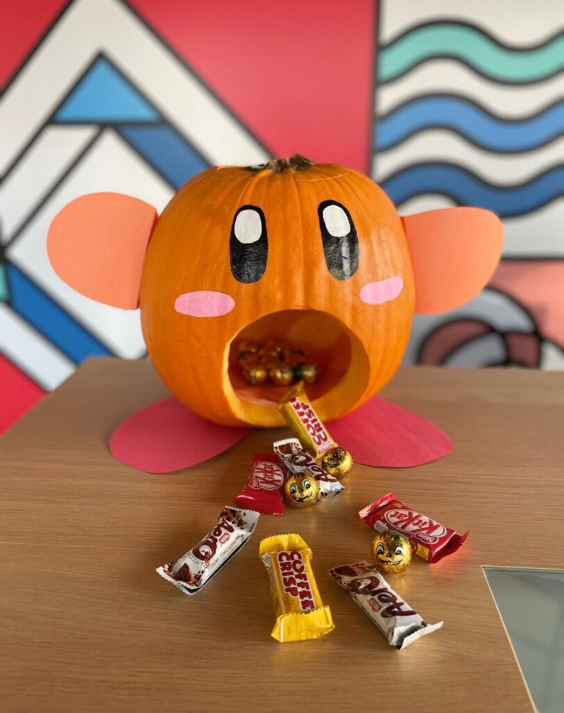 Pumpkin painted as Kirby dispensing Halloween candy.