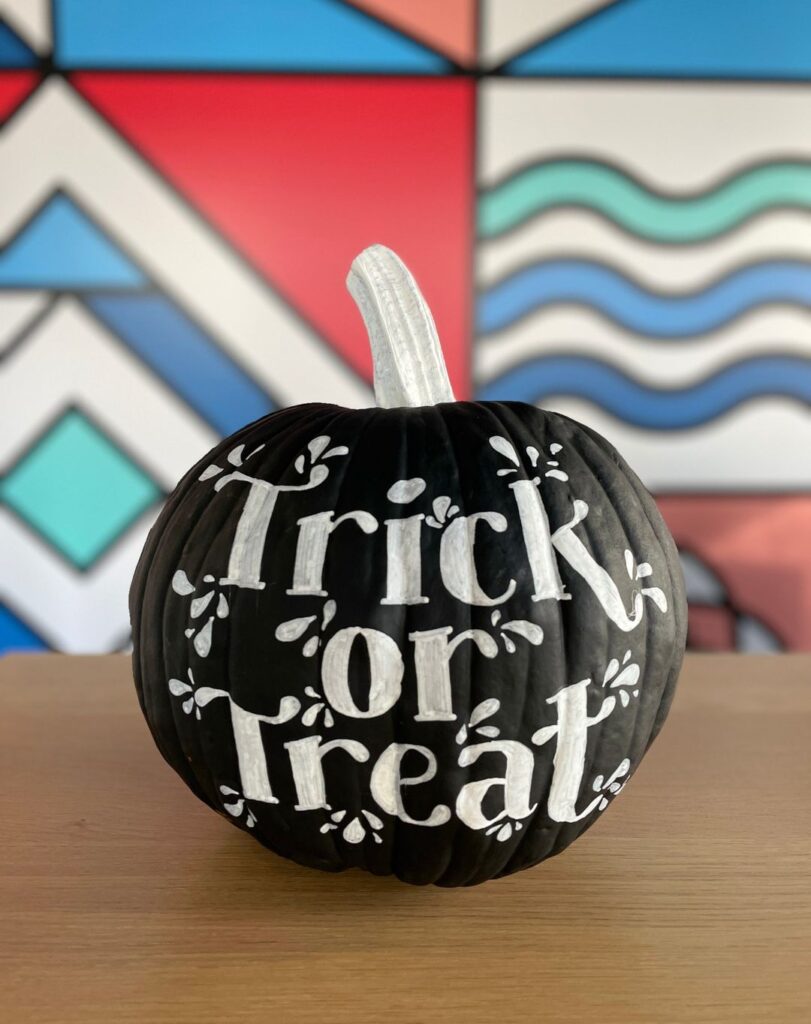 Black pumpkin painted with "Trick or Treat" message.