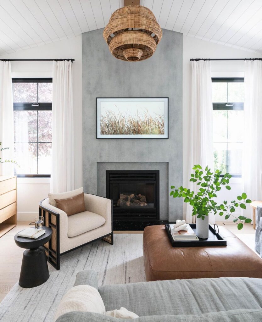 Coastal-inspired living room with concrete fireplace, rattan chandelier, and natural accents.