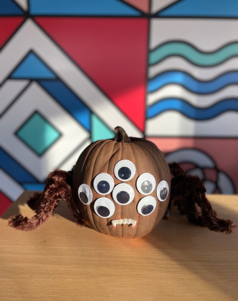 Pumpkin decorated as spider with multiple eyes and legs.