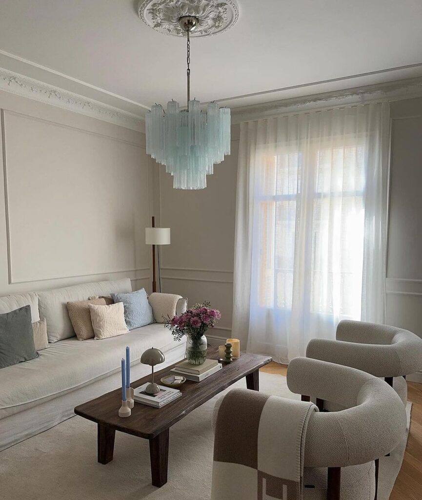 Minimalist living room with blue chandelier and neutral furniture.