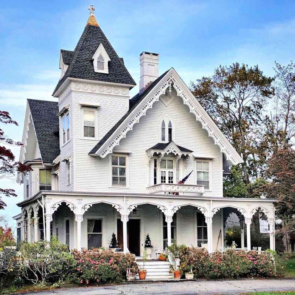 "White Gothic Revival mansion with wraparound porch and pointed tower"